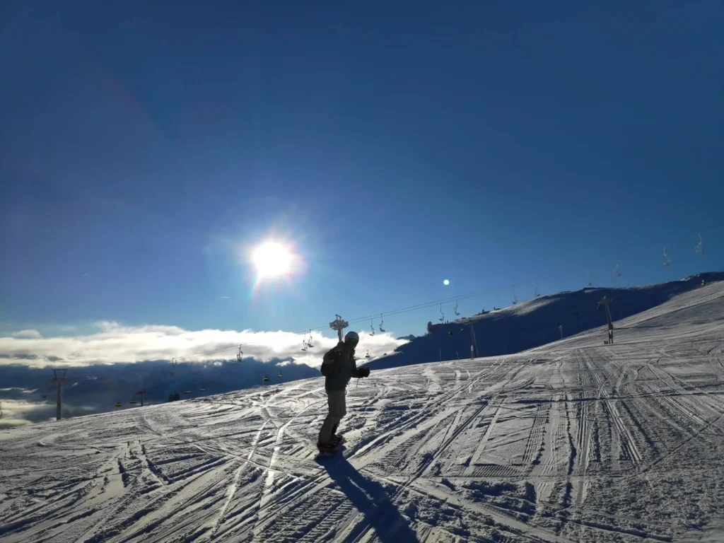 Snowboarder op een piste in het Zillertal met in de achtergrond blauwe lucht, zon en een stoeltjeslift